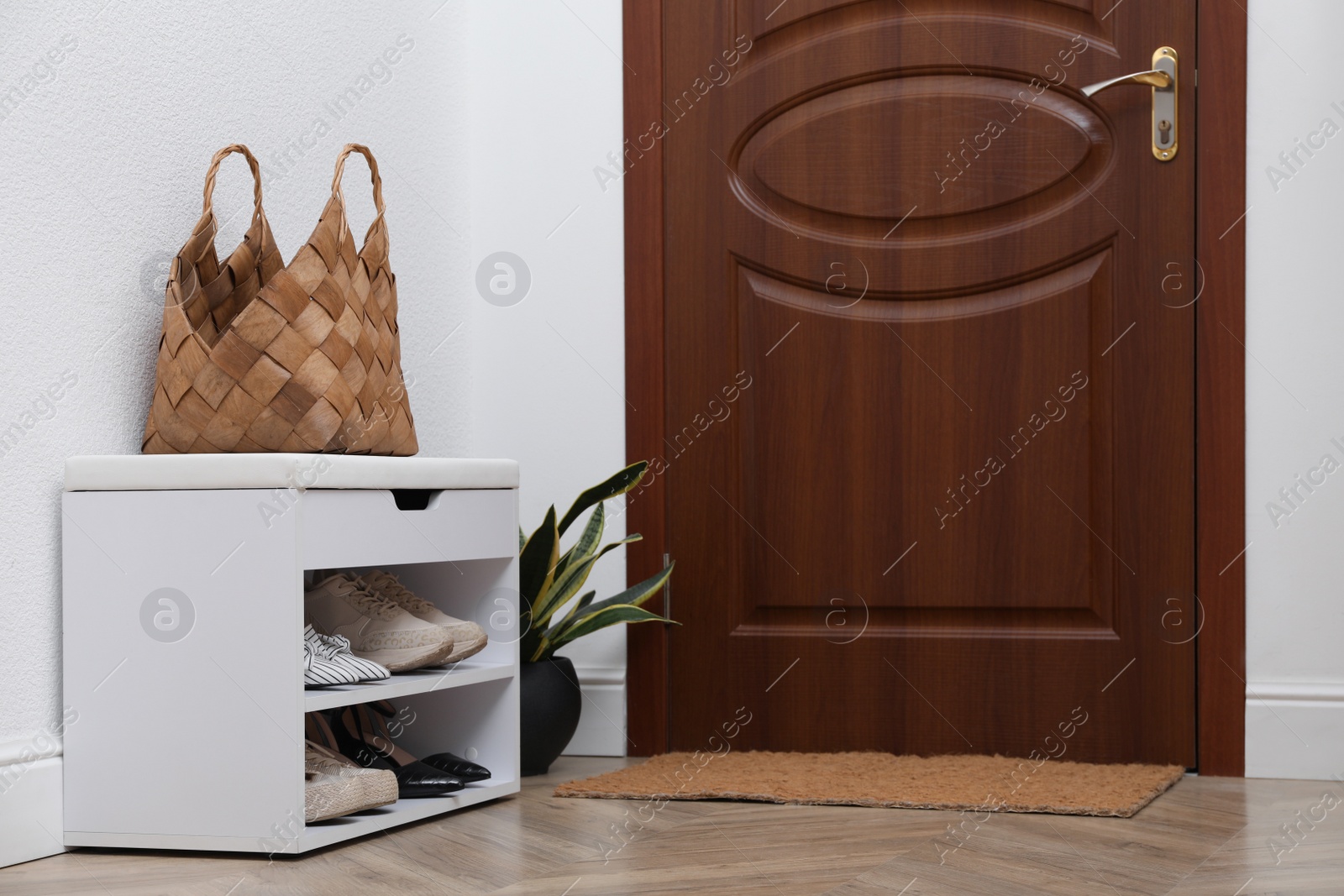 Photo of Shelving unit with shoes, houseplant and door mat in hall