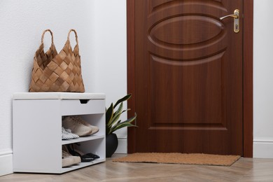 Photo of Shelving unit with shoes, houseplant and door mat in hall