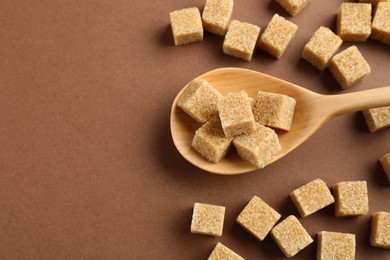 Photo of Brown sugar cubes and spoon on color background, flat lay. Space for text