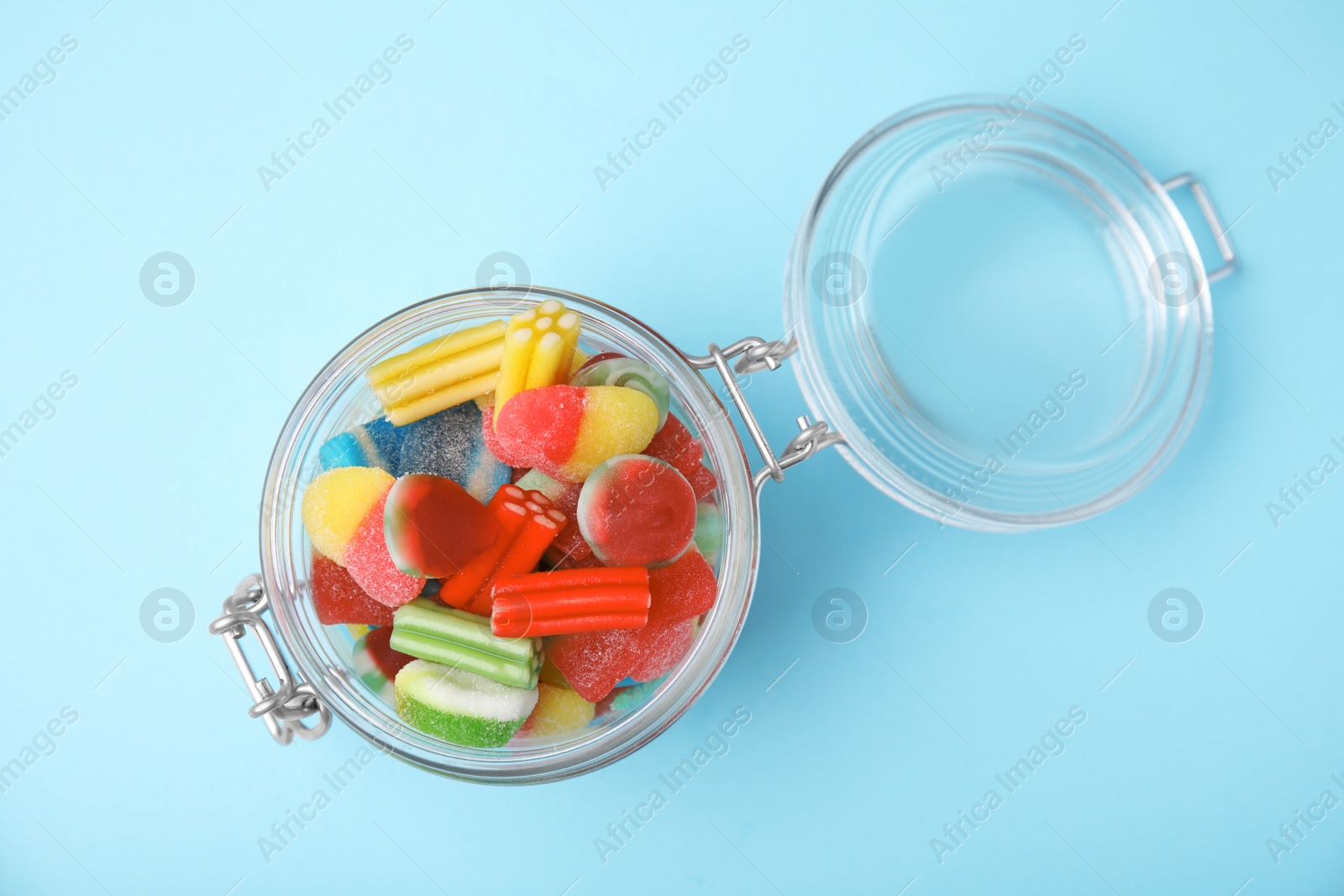 Photo of Tasty colorful jelly candies in glass jar on light blue background, top view