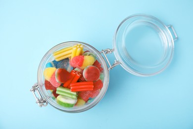Photo of Tasty colorful jelly candies in glass jar on light blue background, top view