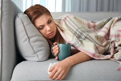 Photo of Sick woman with cup of hot drink lying on sofa at home. Influenza virus