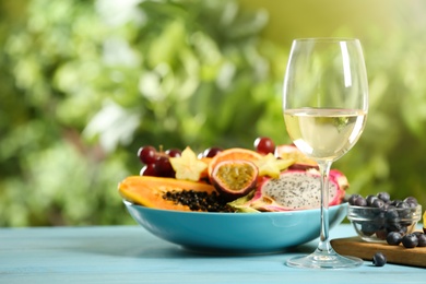 Delicious exotic fruits and wine on light blue wooden table, space for text