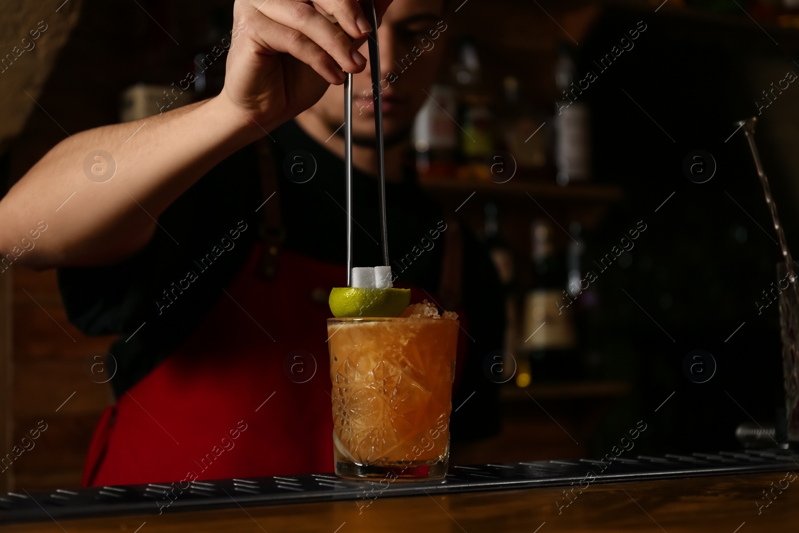 Photo of Bartender decorating glass of fresh alcoholic cocktail at bar counter, closeup