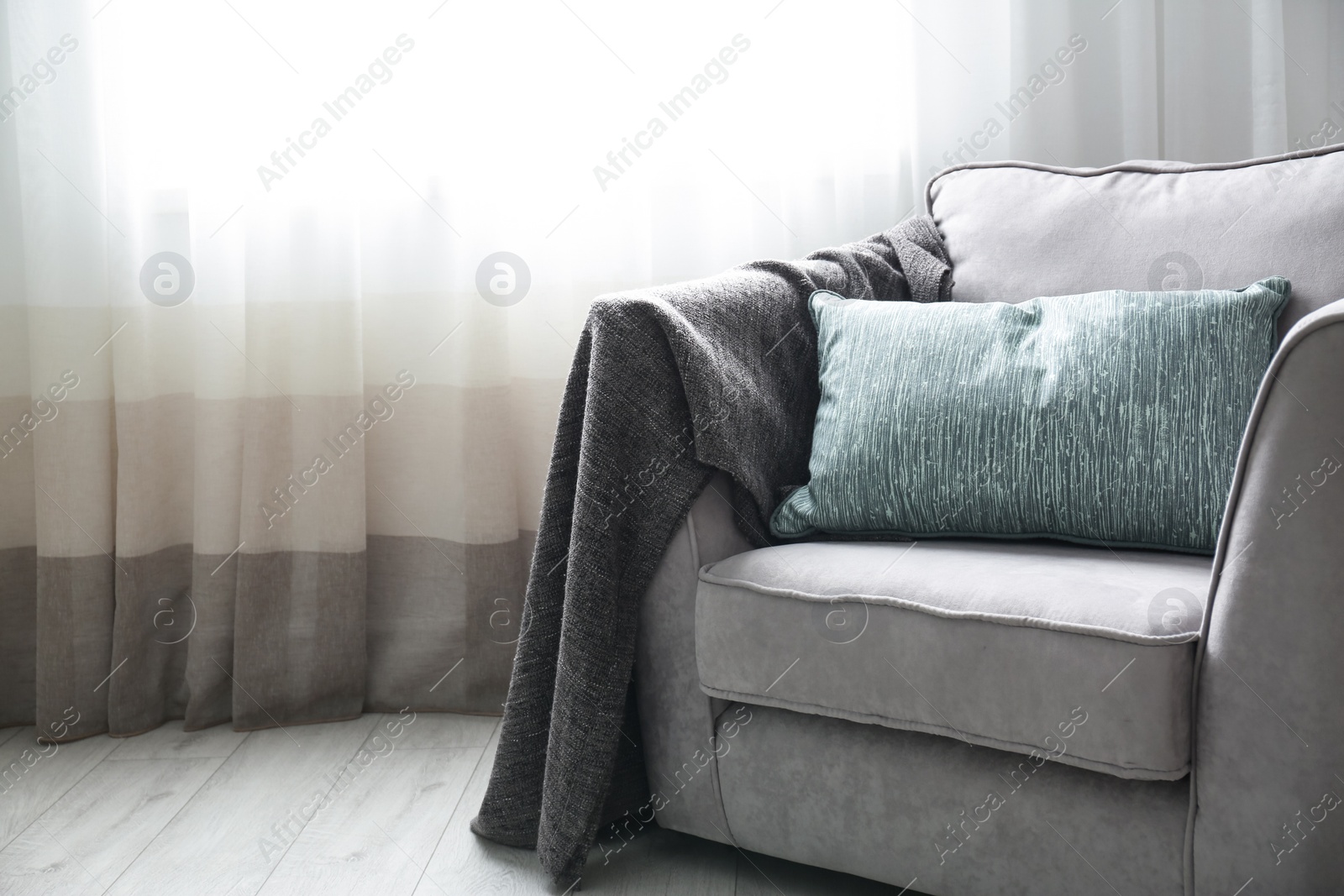 Photo of Cozy armchair with pillows and plaid near window in room. Interior design