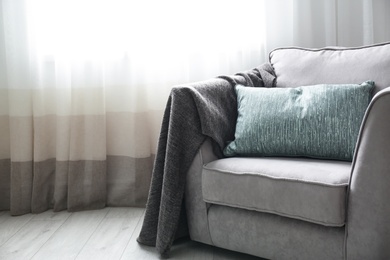 Photo of Cozy armchair with pillows and plaid near window in room. Interior design