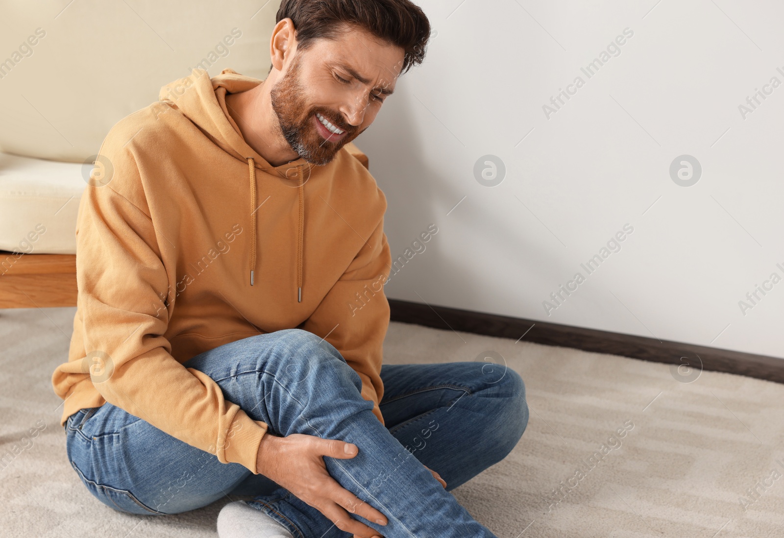 Photo of Man suffering from leg pain on carpet indoors