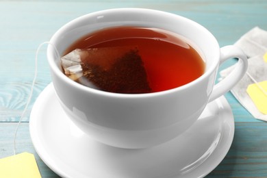 Photo of Tea bag in cup with hot drink on light blue wooden table, closeup