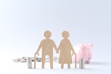 Photo of Pension savings. Figure of senior couple, coins and piggy bank on white background