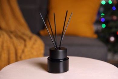 Photo of Aromatic reed air freshener on white wooden side table in cozy room