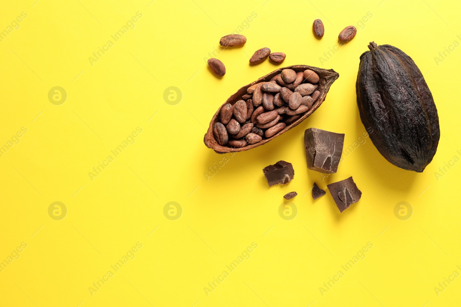 Photo of Cocoa pods with beans and chocolate pieces on yellow background, flat lay. Space for text