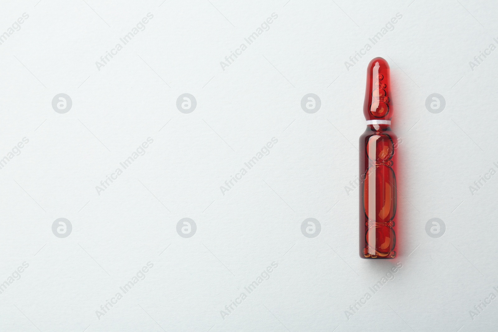 Photo of Glass ampoule with liquid on white background, top view. Space for text