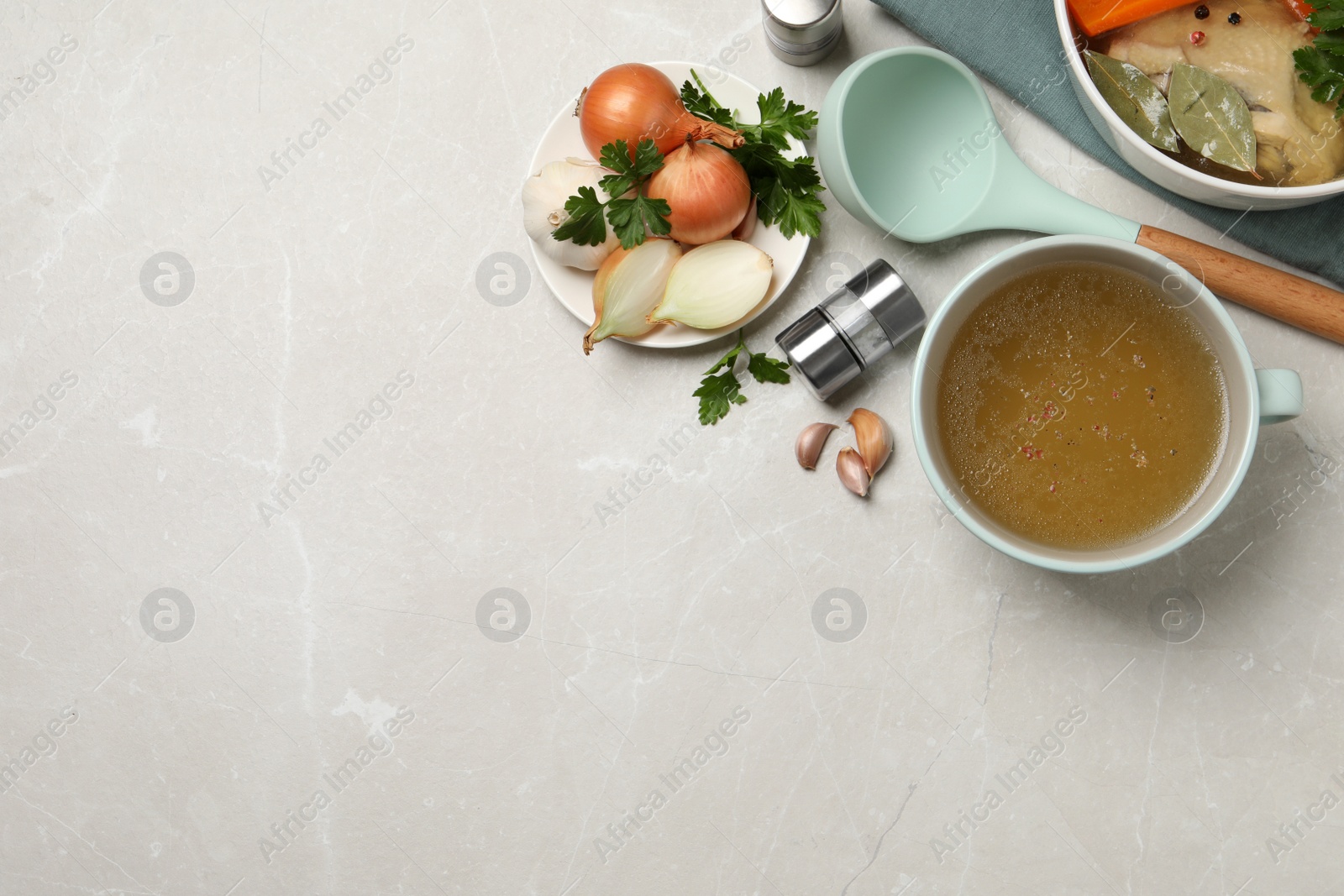 Photo of Hot delicious bouillon and ingredients on light grey table, flat lay. Space for text