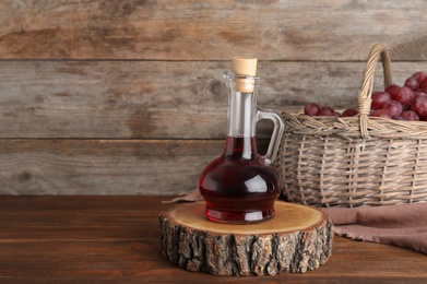 Photo of Composition with glass jug of wine vinegar and fresh grapes in basket on wooden table. Space for text
