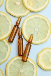 Skincare ampoules with vitamin C and slices of lemon on light blue background, flat lay