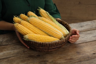 Photo of Woman with bunch of corn cobs at wooden table, closeup
