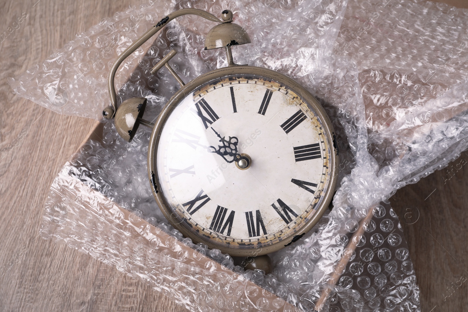 Photo of Vintage alarm clock with bubble wrap and packaging foam in cardboard box on wooden table, above view