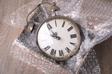 Vintage alarm clock with bubble wrap and packaging foam in cardboard box on wooden table, above view