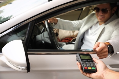 Man sitting in car and paying with credit card at gas station, focus on hand