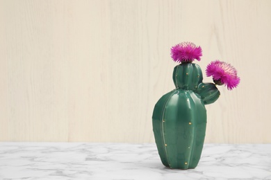 Trendy cactus shaped ceramic vase with flowers on table against wooden background