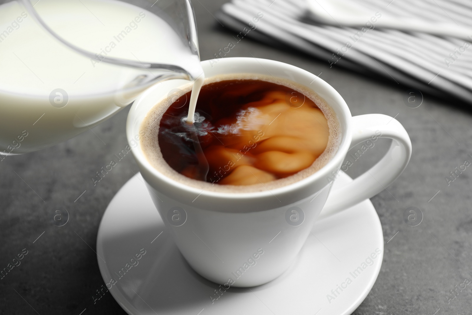 Photo of Pouring milk into cup of hot coffee on grey table, closeup