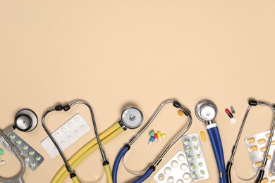 Stethoscopes and pills on beige background, flat lay. Space for text