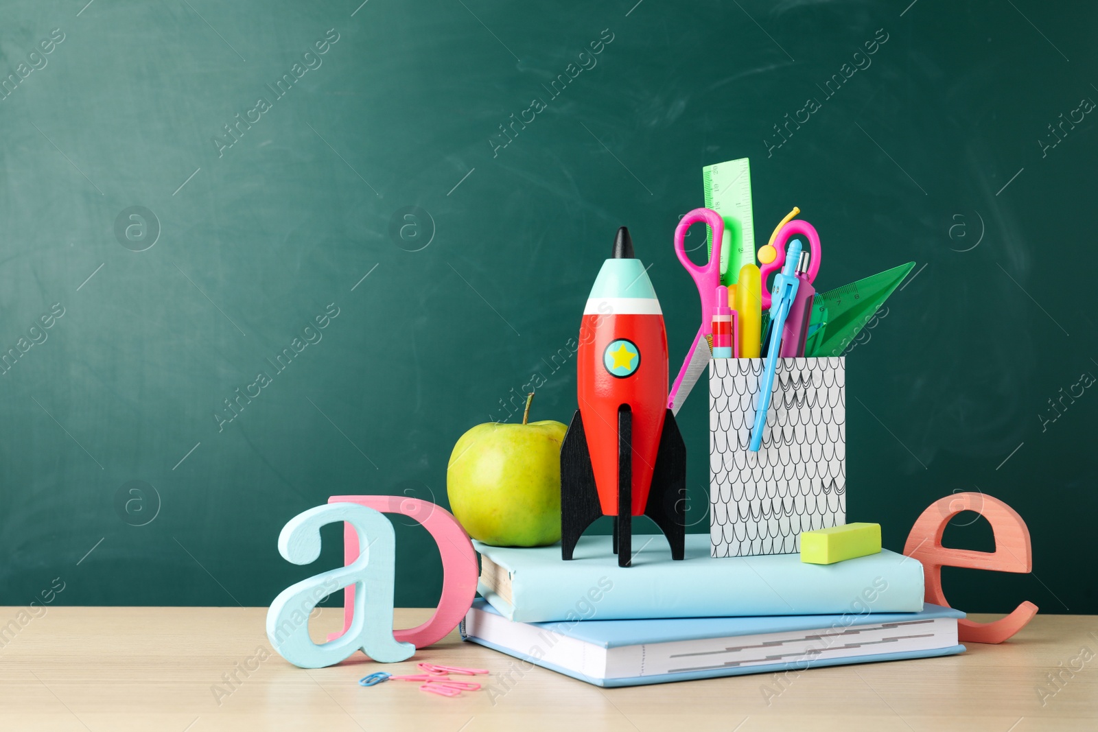 Photo of Bright toy rocket and school supplies on wooden desk. Space for text