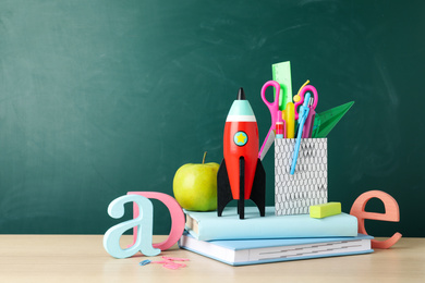 Bright toy rocket and school supplies on wooden desk. Space for text