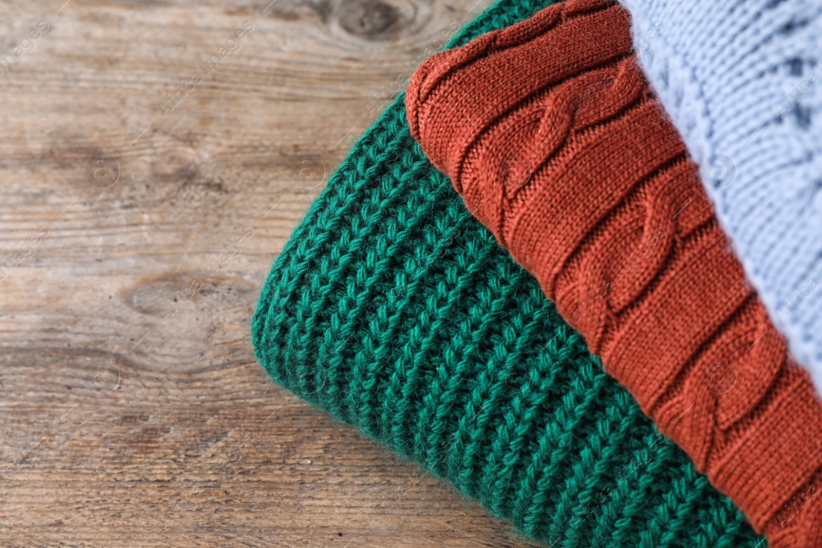 Image of Stack of folded warm sweaters on wooden table, closeup