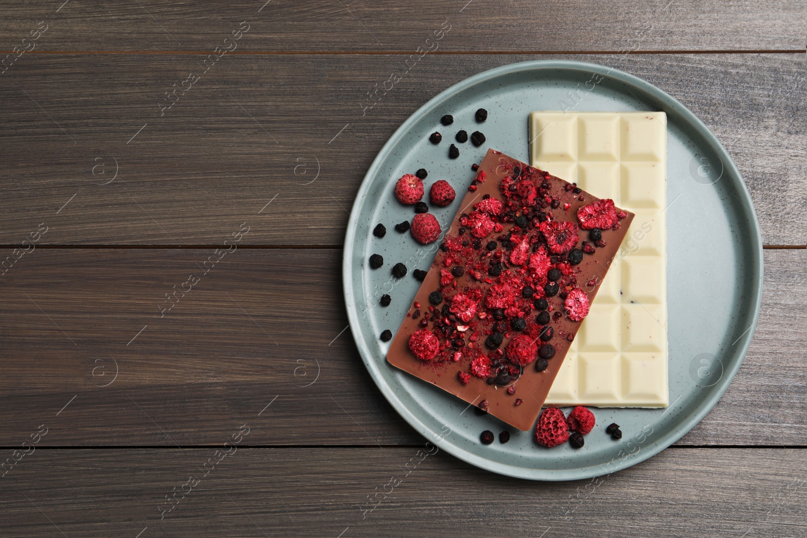 Photo of Plate and different chocolate bars with freeze dried fruits on wooden table, top view. Space for text