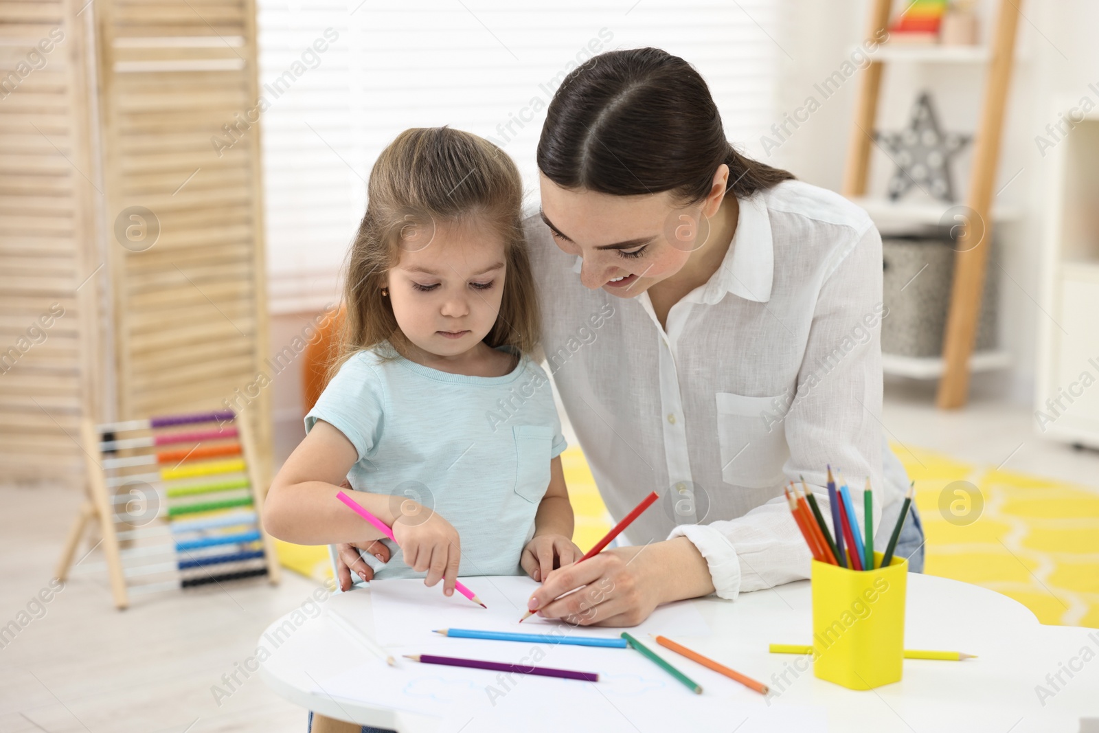 Photo of Mother and her little daughter drawing with colorful pencils at home