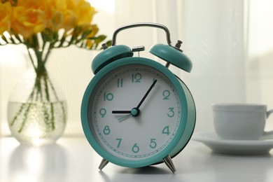 Photo of Alarm clock on white table indoors. Morning time