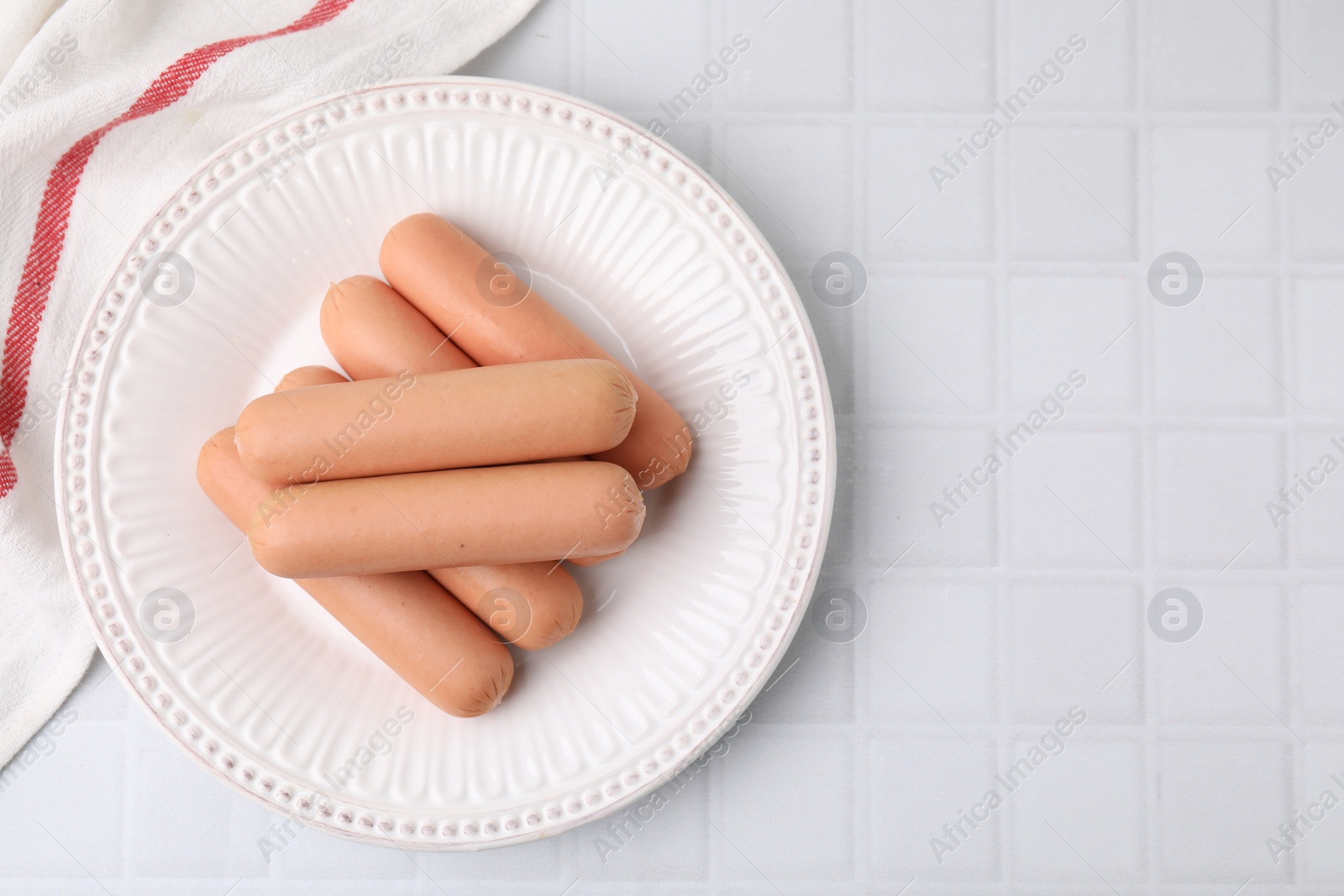 Photo of Delicious boiled sausages on white tiled table, top view. Space for text