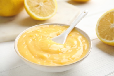 Delicious lemon curd in bowl on white wooden table, closeup