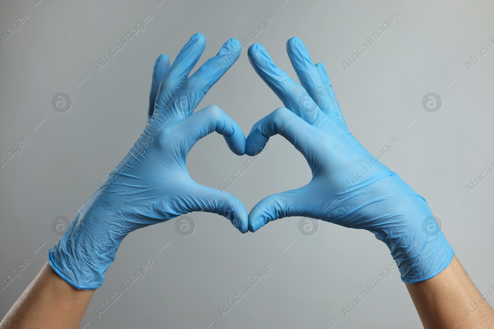 Photo of Doctor wearing light blue medical gloves making heart gesture on grey background, closeup