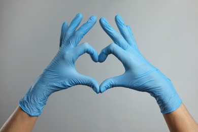 Doctor wearing light blue medical gloves making heart gesture on grey background, closeup
