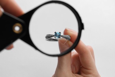 Jeweler examining topaz ring with magnifying glass on white background, closeup