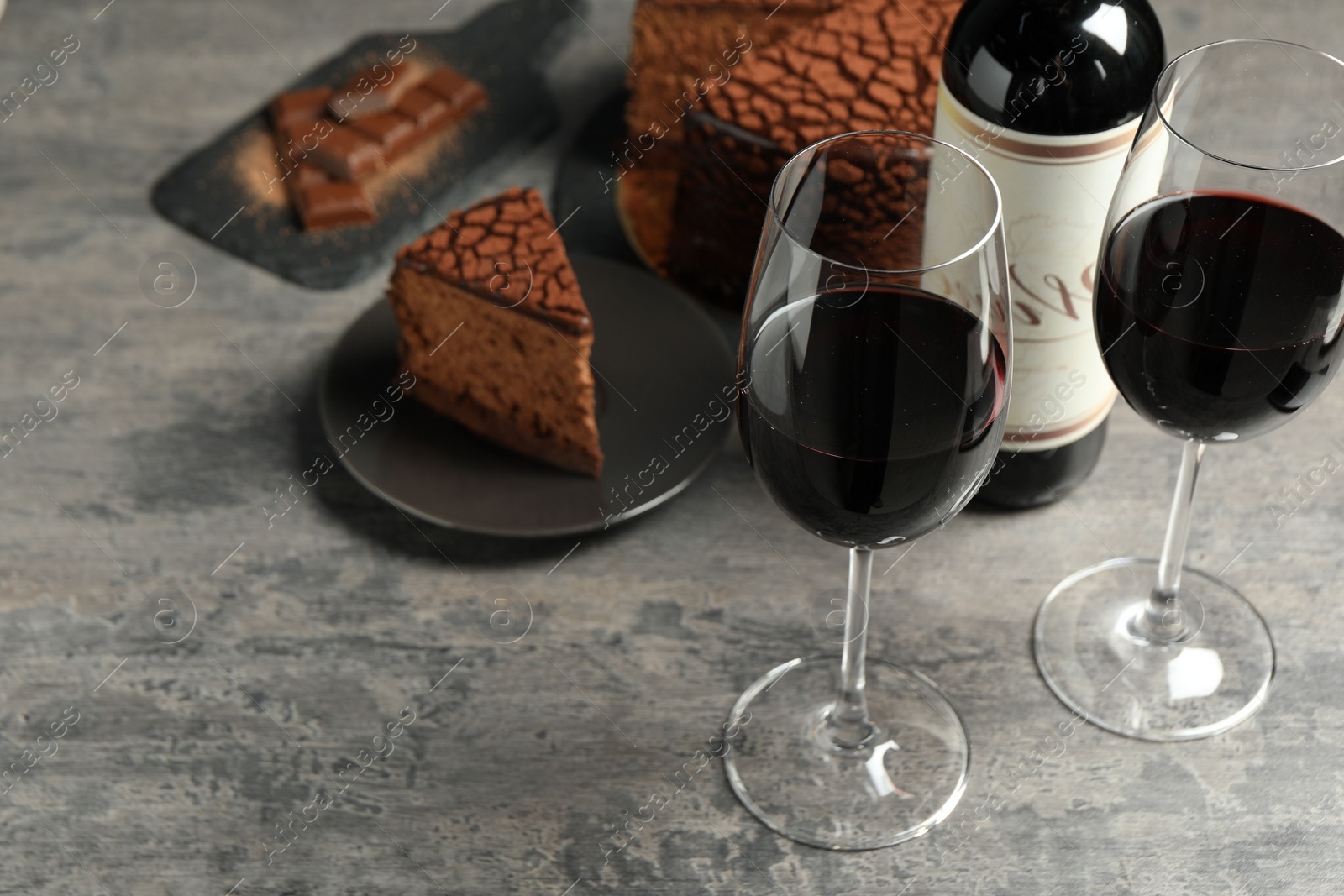 Photo of Delicious chocolate truffle cake and red wine on grey textured table