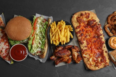 Burger, pizza and other fast food on black table, flat lay
