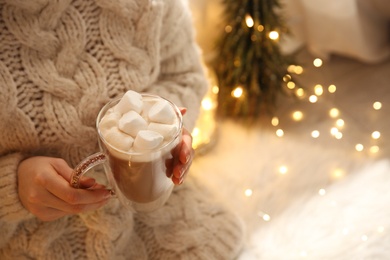 Photo of Woman holding cup of hot drink with marshmallow indoors, closeup