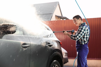 Worker cleaning automobile with high pressure water jet at car wash