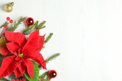 Photo of Flat lay composition with poinsettias (traditional Christmas flowers) and holiday decor on white wooden table. Space for text