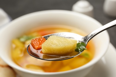 Spoon with fresh homemade chicken soup on blurred background, closeup