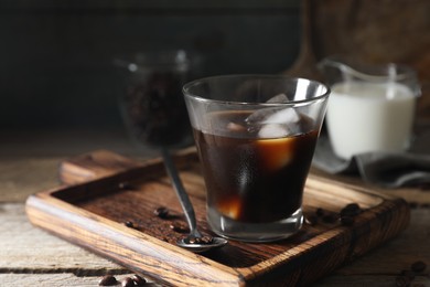 Photo of Glass of delicious iced coffee and beans on wooden table, space for text