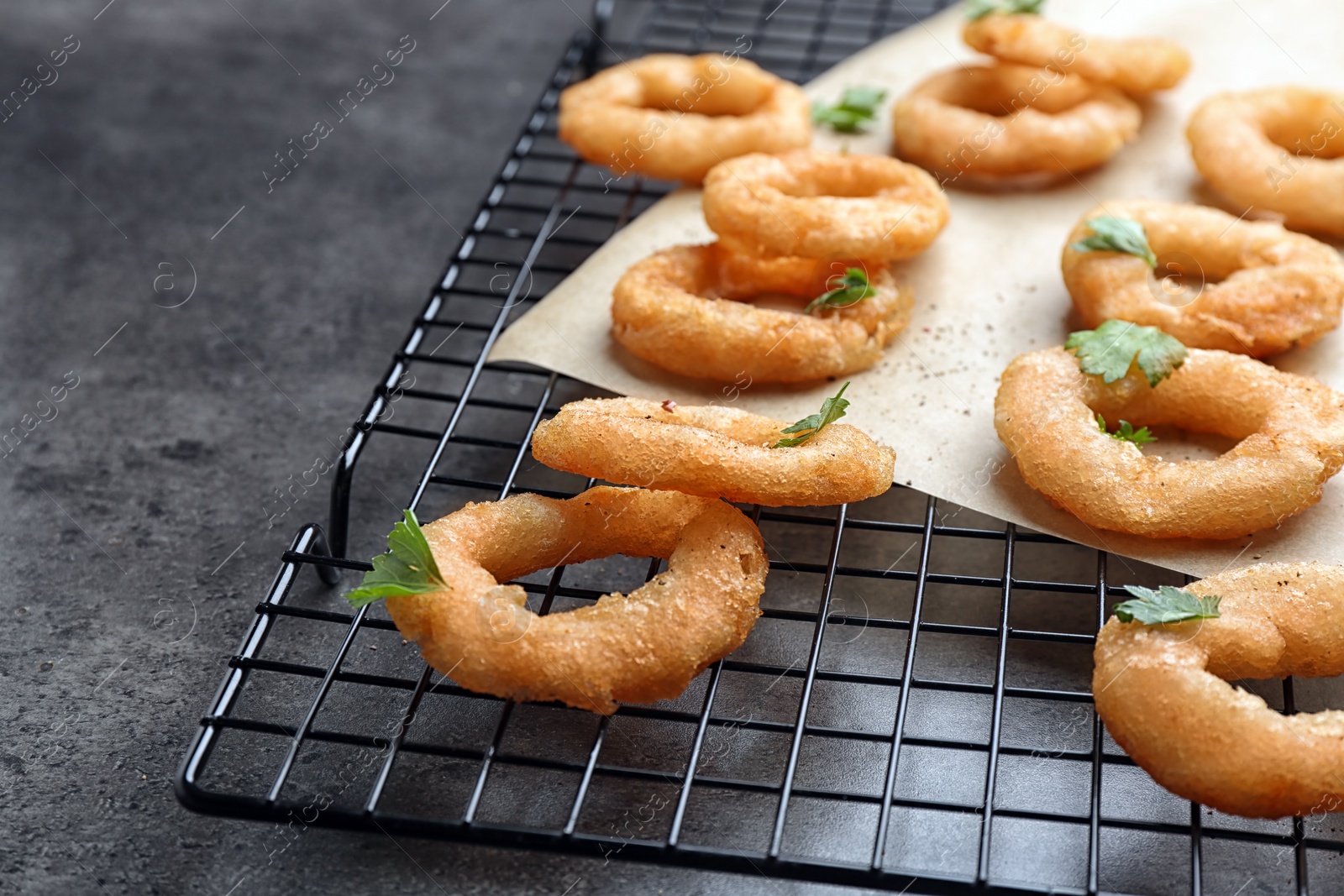 Photo of Cooling rack with fried onion rings on grey background, closeup