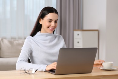 Photo of Happy woman working with laptop at wooden desk in room