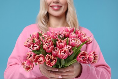 Photo of Happy woman holding beautiful bouquet on light blue background, closeup