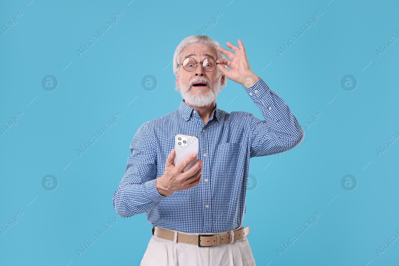 Photo of Portrait of stylish grandpa with glasses using smartphone on light blue background