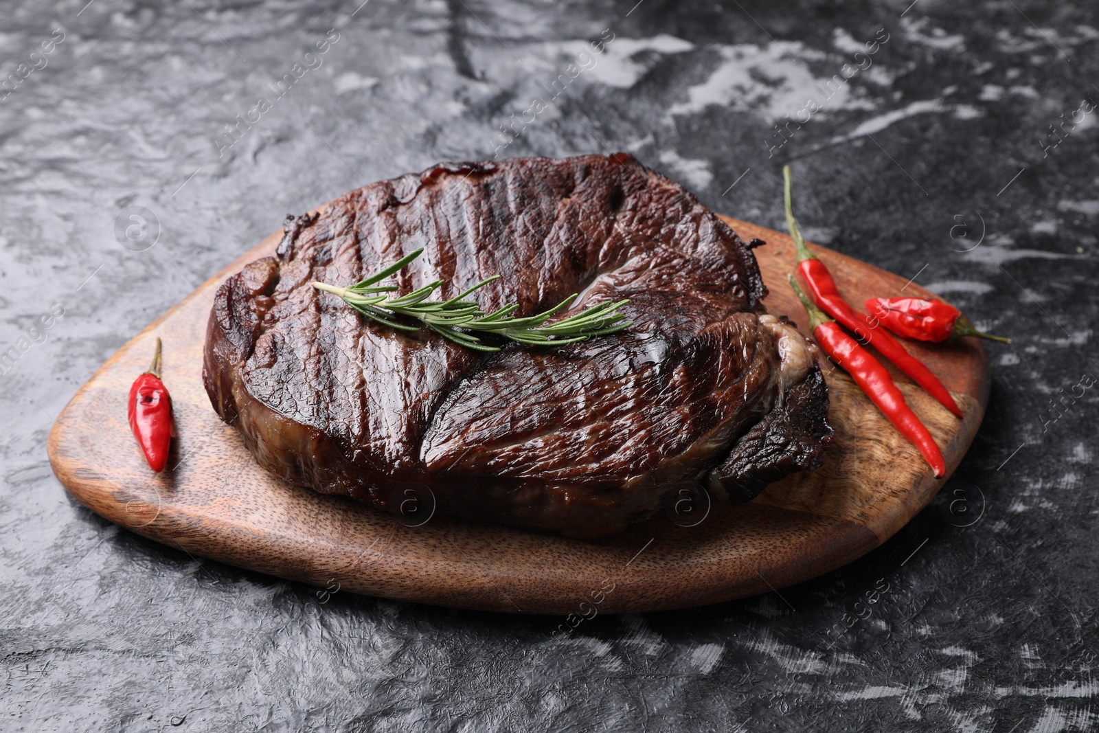 Photo of Delicious fried beef meat with pepper and rosemary on grey textured table, above view