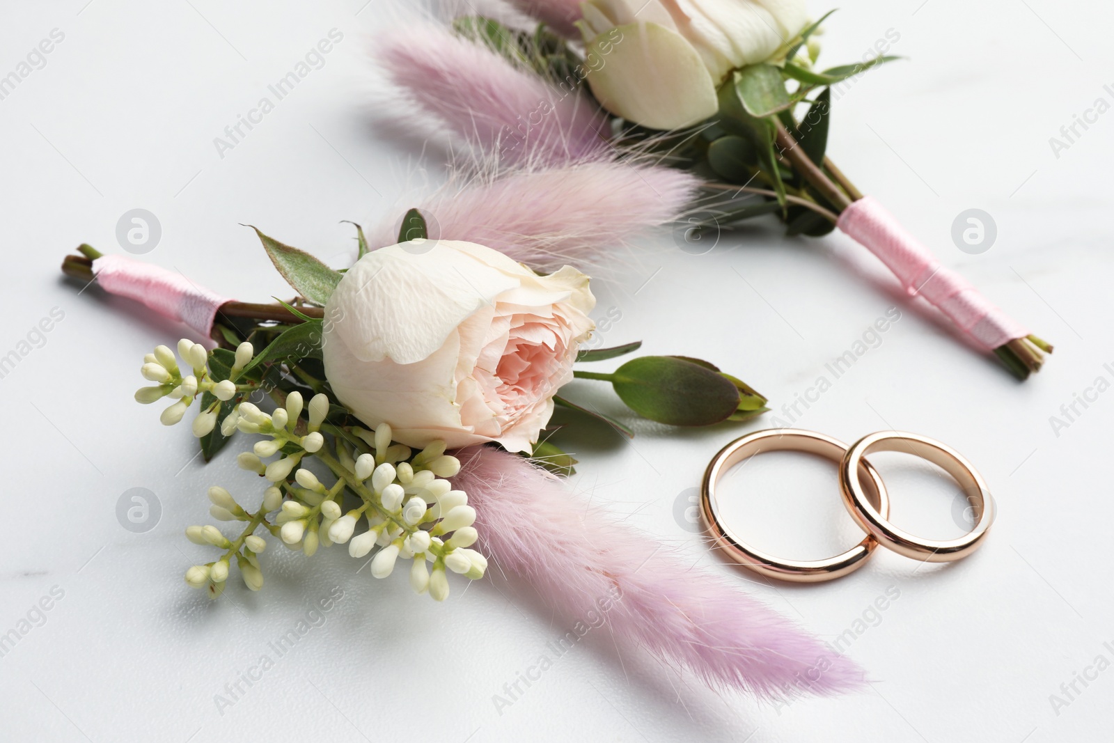 Photo of Small stylish boutonnieres and rings on white marble table